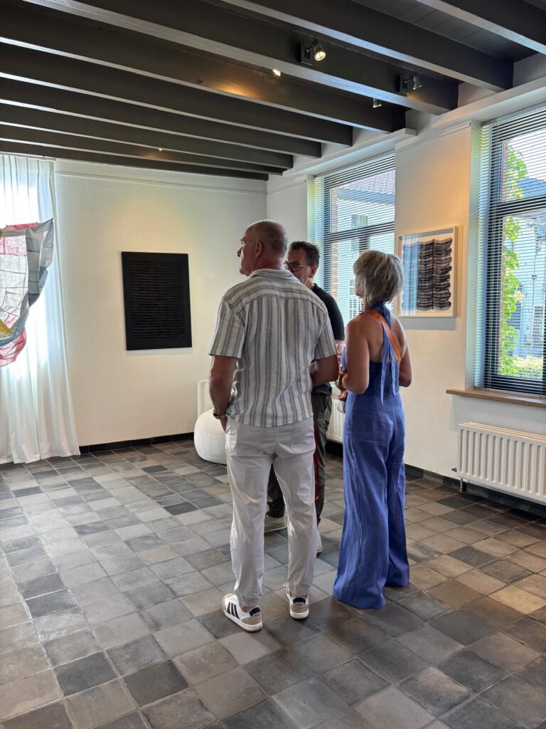Drie bezoekers bekijken een werk aan de wand