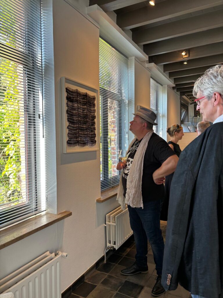 Bezoeker bekijkt een ingelijst textielwerk bij het raam